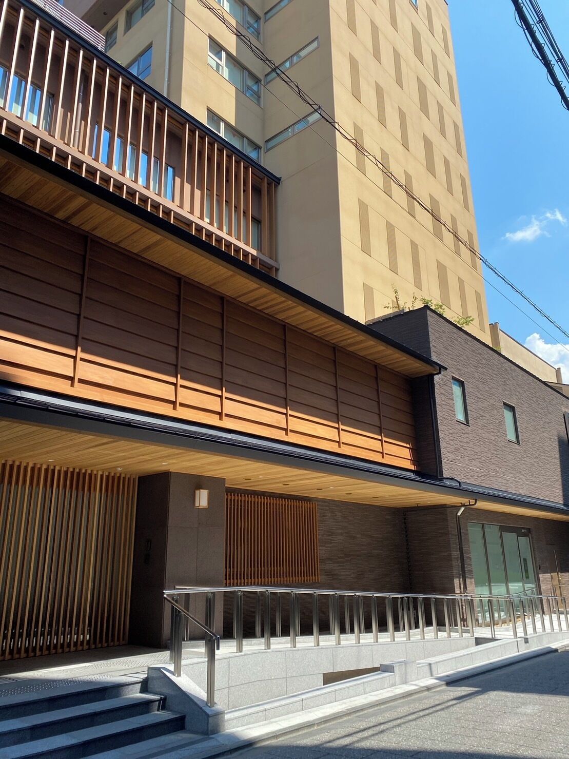 A modern building with a wooden facade, a balcony, and a staircase leading to the entrance.