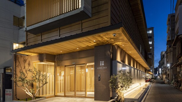 A modern hotel entrance with a wooden facade, a gated entrance, and a well-lit pathway. - RYOKAN GINKAKU KYOTO (Kyoto)