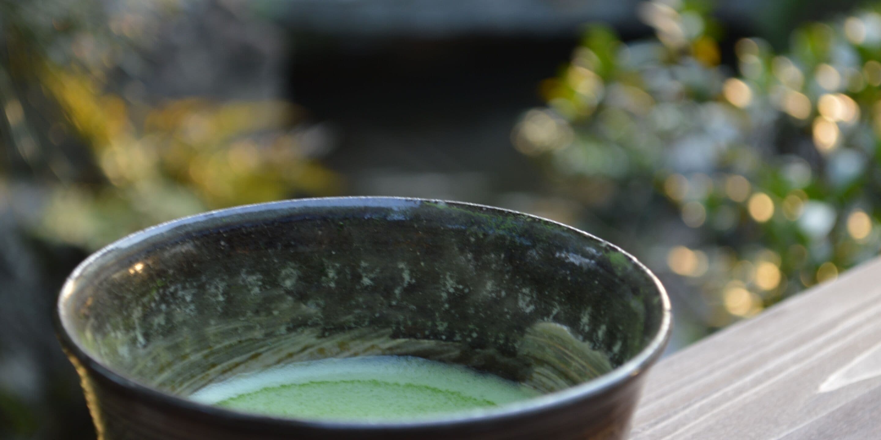 Primer plano de una taza de cerámica con líquido verde, posiblemente una bebida, sobre una superficie de madera.