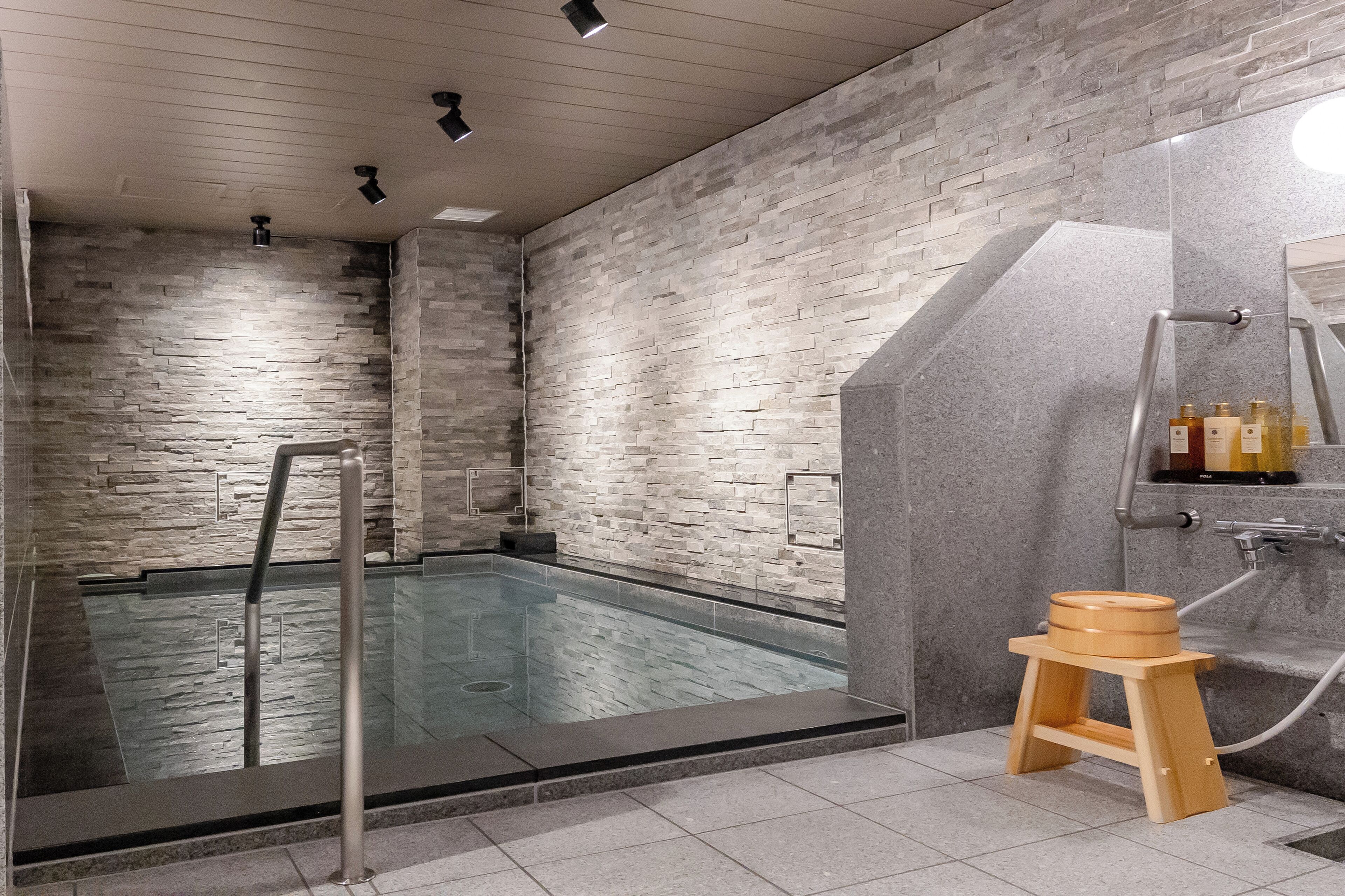 A modern bathroom with a stone wall, a glass-enclosed shower, and a wooden stool.