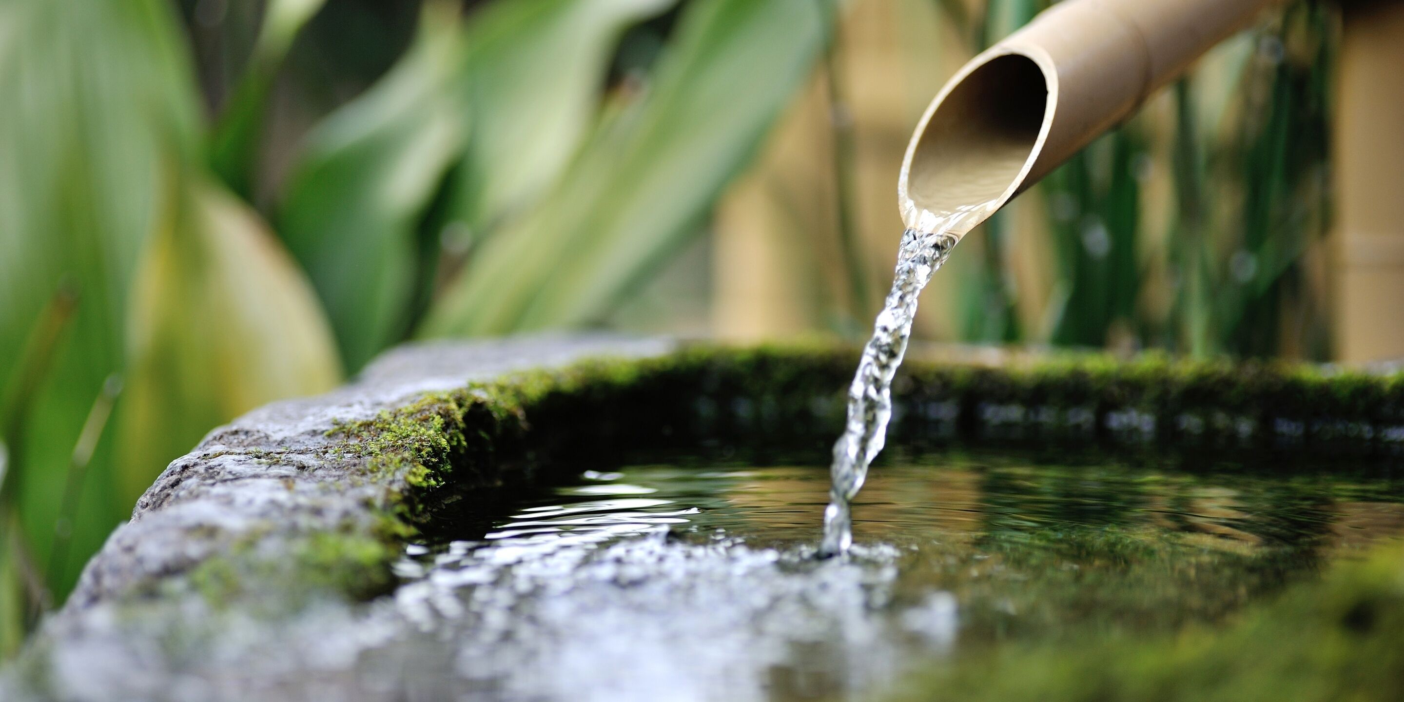 Primer plano de agua que fluye desde un caño metálico curvo hacia una pila de piedra.