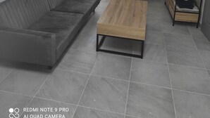 Een moderne woonkamer met een grijze bank, een houten salontafel, een televisie op een houten dressoir, en een wandklok.