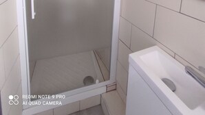 Een badkamer met een douche met glazen wand, een witte wastafel en een spiegel aan de muur.