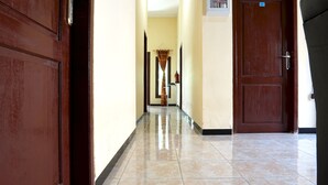A hallway with a tiled floor, wooden doors, and a fire extinguisher mounted on the wall.