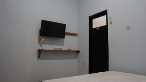 A room with a bed, a mounted TV, a door, and a shelf with a remote control.