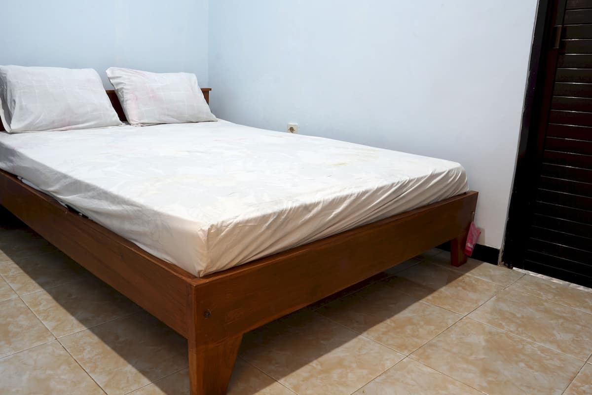 A single bed with a wooden frame and a white mattress in a room with tiled flooring.