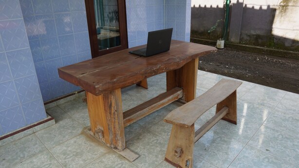 A wooden bench and table with a laptop on it, placed on a tiled floor.