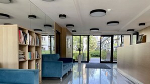 Moderni aula, jossa on sininen sohva, kirjahylly ja lasiovi, joka johtaa ulos.