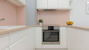 A compact kitchen with white cabinets, a stainless steel oven, a small potted plant, and a bowl of lemons on the countertop.