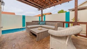 A covered outdoor area with a pool, wooden furniture, and a wicker chair. - Cozy home with private pool! Close to everything! Great dining options! Palm Beach and Hadicurari Beach! (Noord)