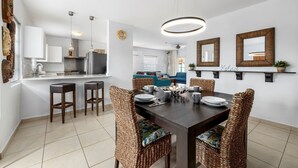 A modern kitchen with white cabinets, a central island with stools, and a dining area with wicker chairs and a dark wooden table. - Cozy home with private pool! Close to everything! Great dining options! Palm Beach and Hadicurari Beach! (Noord)