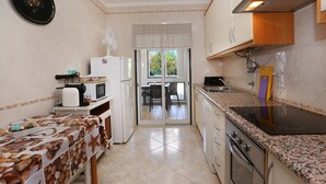 A compact kitchen with a dining area, a refrigerator, microwave, stove, and a window with a view. - Apartment in Condominium with Swimming Pool (Alvor)