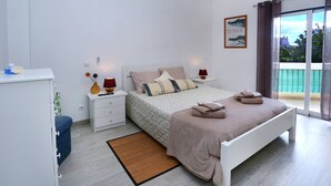 A bedroom with a bed, bedside tables, a nightstand, a window with curtains, and a view of the outside. - Apartment in Condominium with Swimming Pool (Alvor)