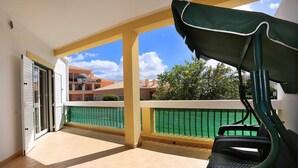 An open balcony with a view of neighboring buildings, a green fence, and a chair. - Apartment in Condominium with Swimming Pool (Alvor)