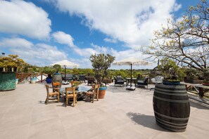 An outdoor patio area with wooden tables and chairs, potted plants, and umbrellas. - Mavi At Hotel (Sariyer)