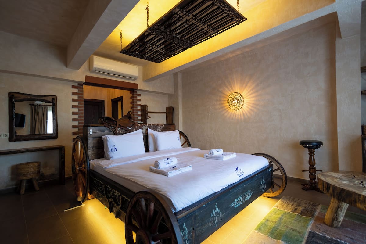 A traditional room with a large bed, a wooden headboard, a wall-mounted mirror, and a unique ceiling light fixture.
