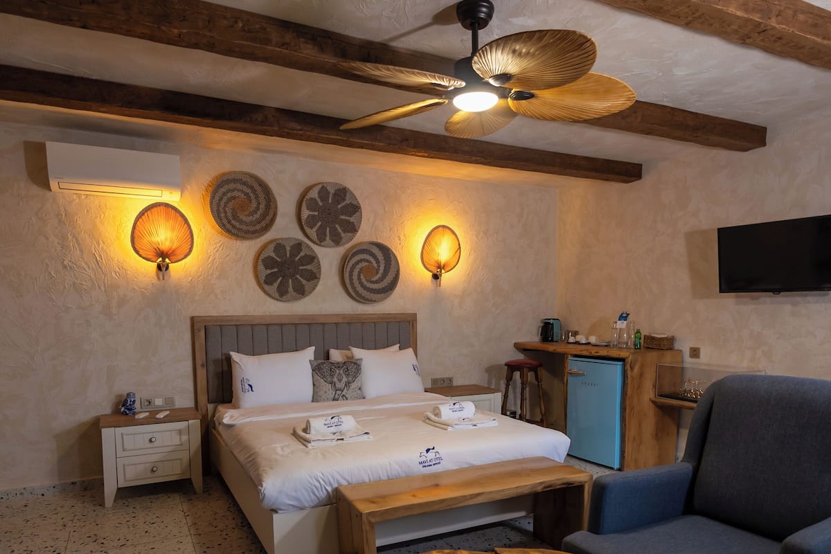 A cozy room with a bed, a wooden coffee table, a blue armchair, a desk with a computer, and a ceiling fan.