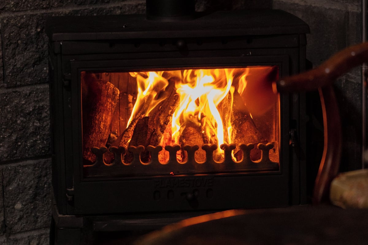 A wood-burning stove with visible flames, set against a stone wall.