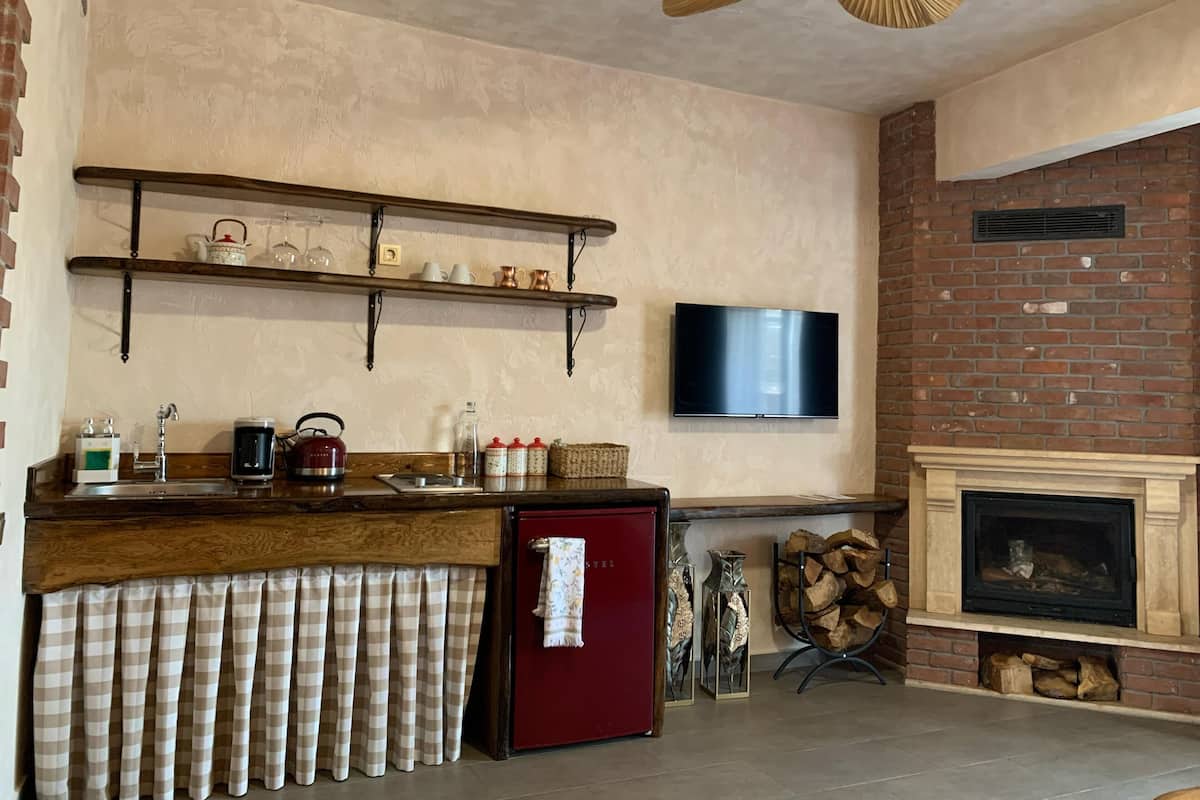 A kitchen with a wooden counter, a refrigerator, a television mounted on the wall, and a fireplace.
