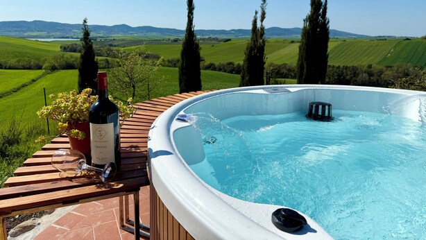 A hot tub with a wooden deck, a bottle of wine, and a glass on the table, overlooking a scenic landscape with rolling hills and tall trees. - A magnificent Tuscan farmhouse, surrounded by greenery between the sea and the hills (Pomaia)