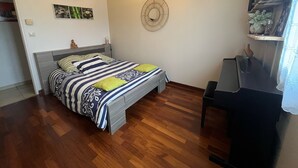 A bedroom with a bed, a desk, a chair, a ceiling fan, and a wall-mounted TV.