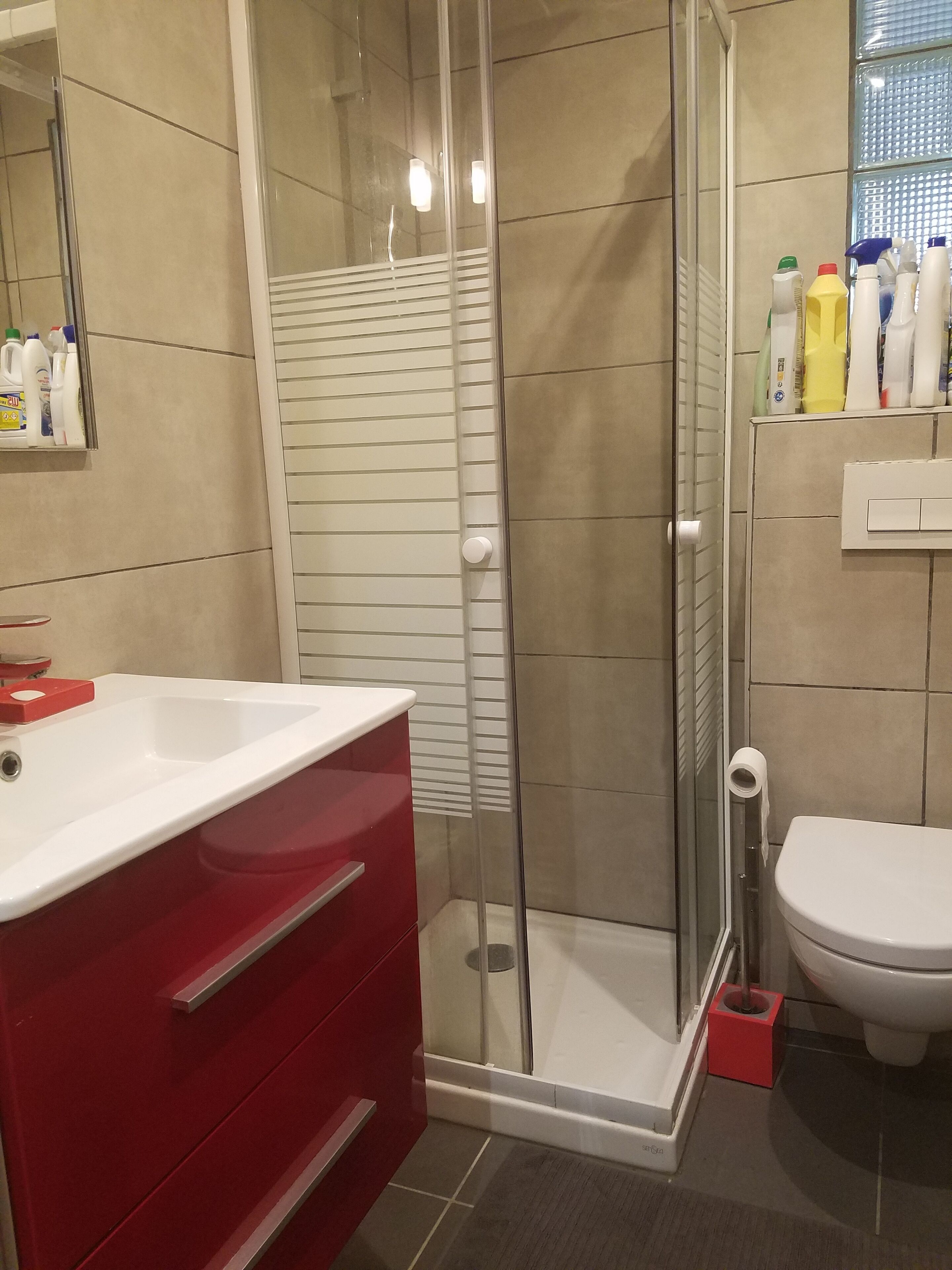Kylpyhuoneessa on lasiseinällä varustettu suihku, punainen allaskaappi, jossa on valkoinen allas, sekä wc.