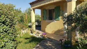 A house with a covered porch, green shutters, and a garden with various plants.