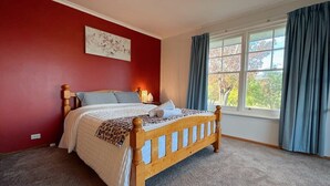 Un dormitorio con cama de madera, pared roja, ventana con cortinas y suelo alfombrado.