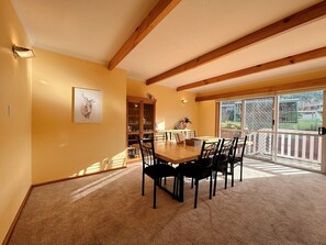A dining area with a wooden table and chairs, a bookshelf, and a large window with a view of a fenced yard.