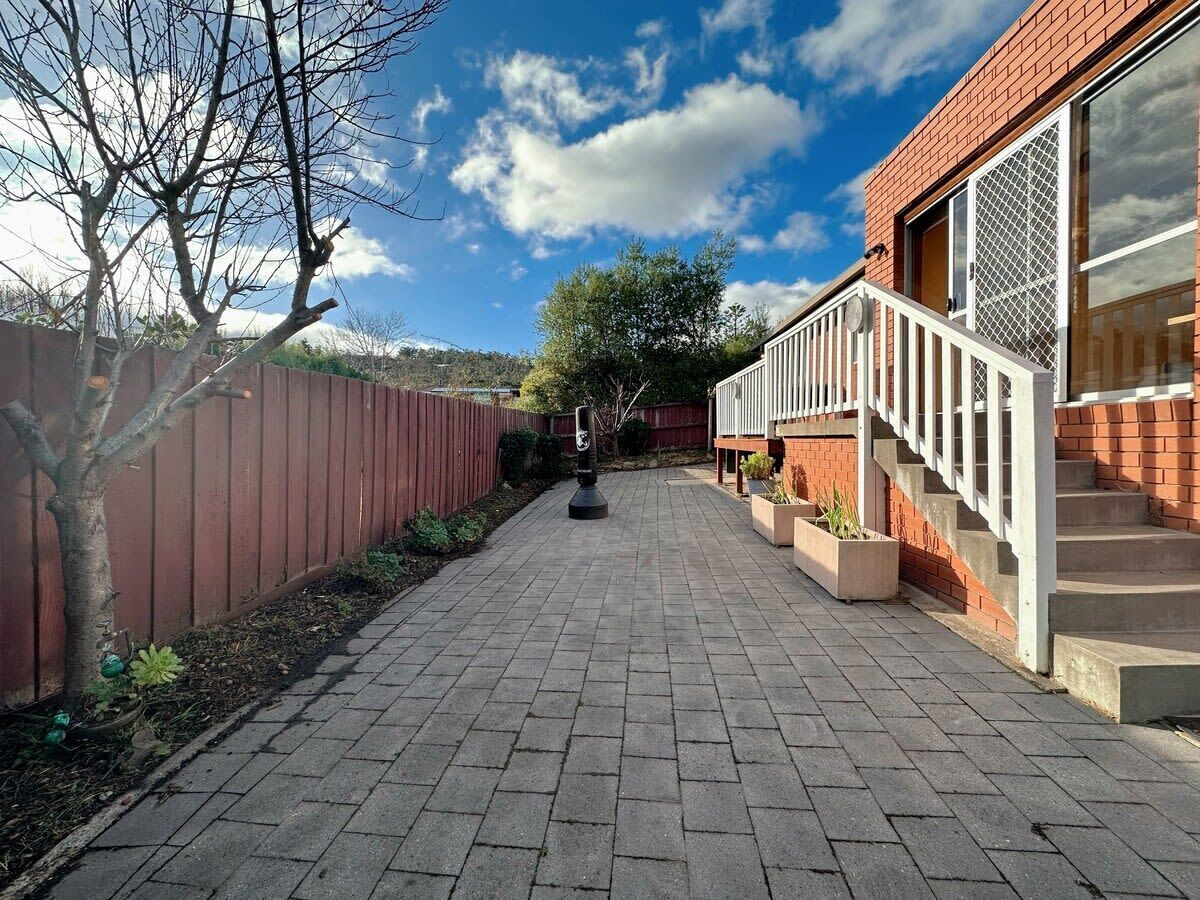 A paved pathway leading to a building with a red brick exterior, a white railing, and a clear sky.
