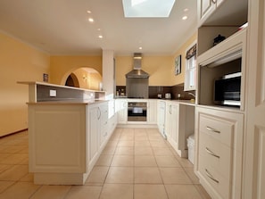 A modern kitchen with white cabinetry, a central island, a built-in oven, and a skylight.