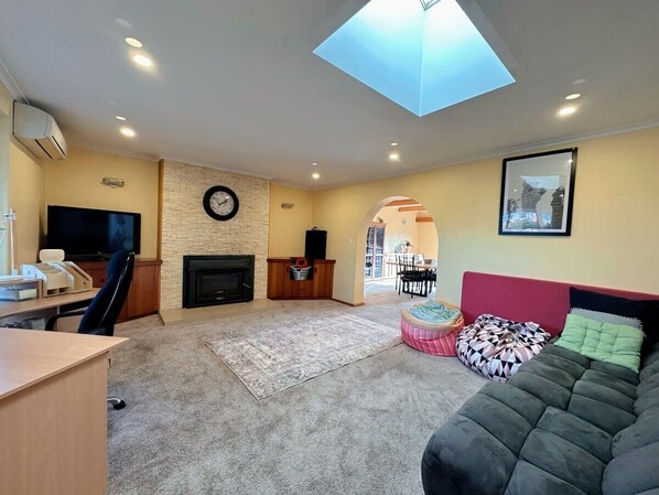 A living room with a fireplace, a TV, a desk, a sofa, and a skylight.