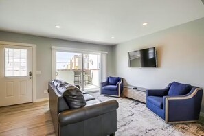 Una sala de estar con un sofá de cuero negro, un sillón azul y un televisor de pantalla plana montado en la pared.