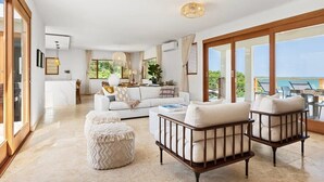 Un amplio salón con un sofá blanco, dos sillones y una mesa de centro. Una ventana grande ofrece vistas al exterior.