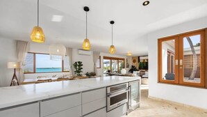 Una cocina moderna con una isla grande, iluminación colgante y vistas al mar.
