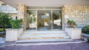 Une entrée d’immeuble avec une façade en pierre, une porte en verre et un escalier menant à un espace abrité.