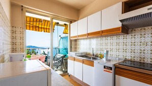 Une cuisine avec des armoires blanches, un four encastré et une grande fenêtre donnant sur un balcon.