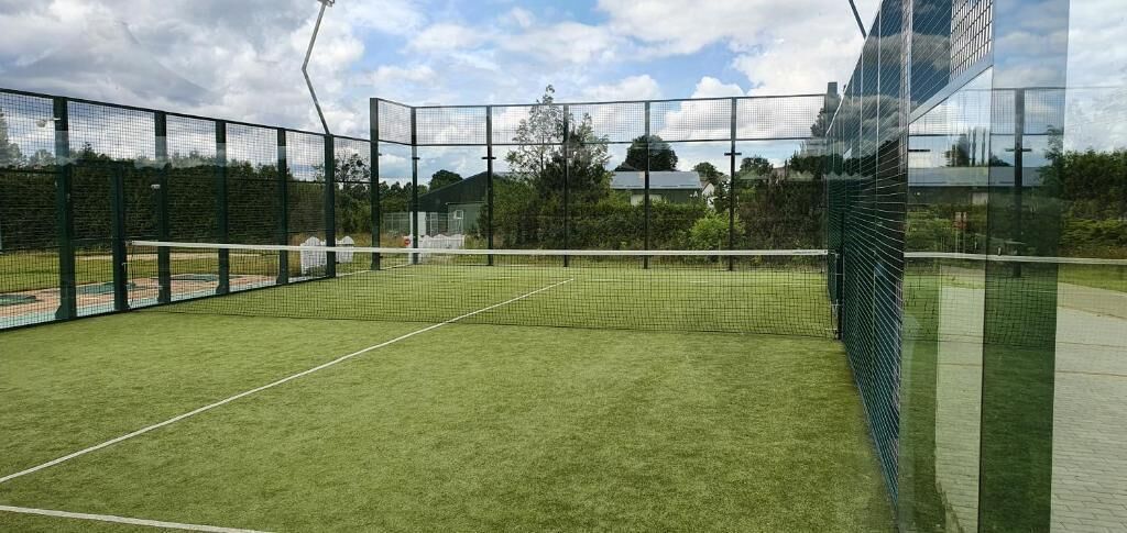 A tennis court with a net, surrounded by a fence, and a clear sky in the background.