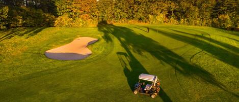 A golf course with a sand bunker and a golf cart.