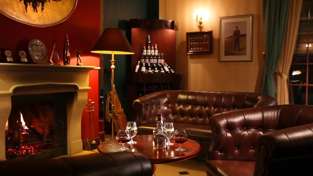Una sala de estar acogedora con chimenea, sofá de cuero y una mesa con vasos.