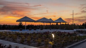 Zona ajardinada con tres sombrillas, una piscina y un jardín bien cuidado.
