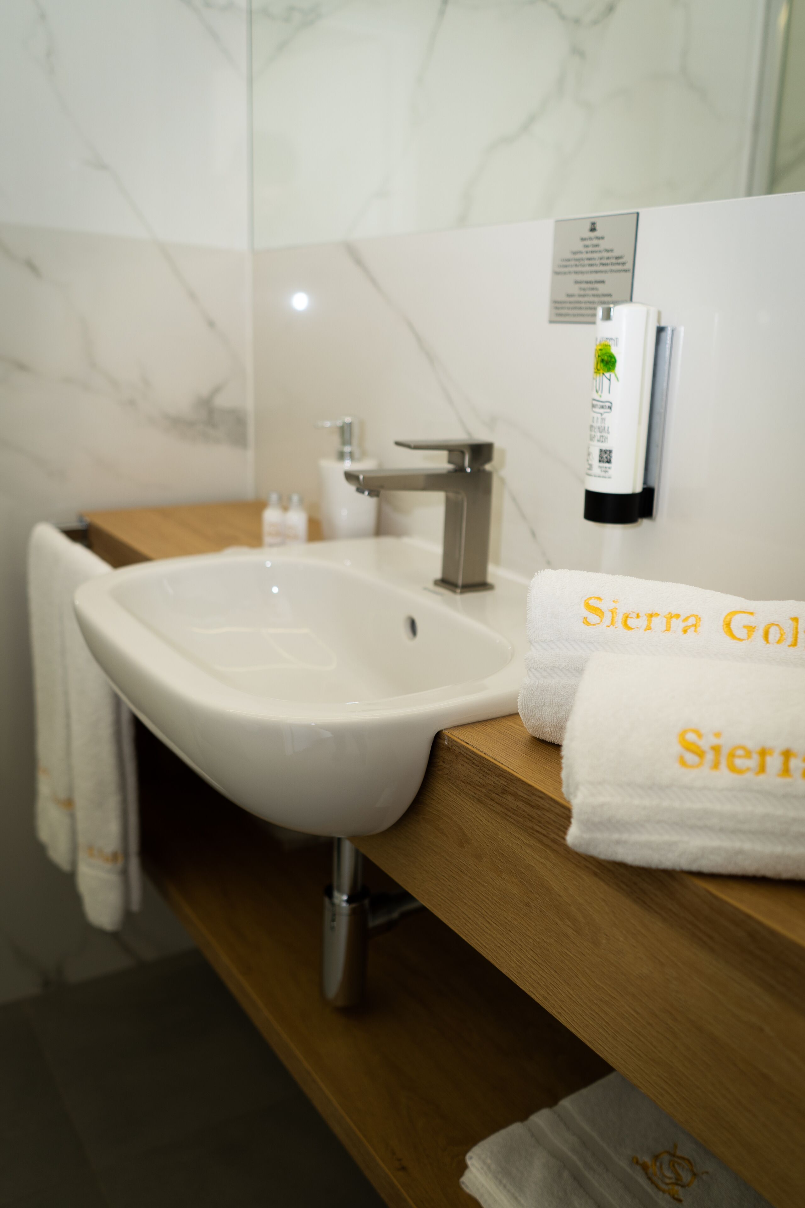 A bathroom with a white sink, a wooden countertop, and two white towels with embroidered text.