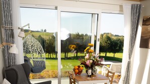 Habitación de hotel con dos camas, una mesa de comedor con sillas, un sillón colgante y vistas a un jardín a través de una puerta de cristal.