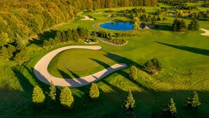 Vista aérea de un campo de golf con búnkeres de arena, un estanque y árboles densos.