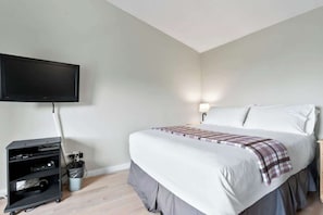 A bedroom with a bed, a TV mounted on the wall, a bedside table with a lamp, and a black entertainment unit with cables.