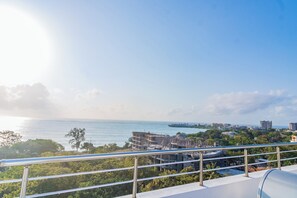 A balcony with a view of the sea, buildings, and greenery.