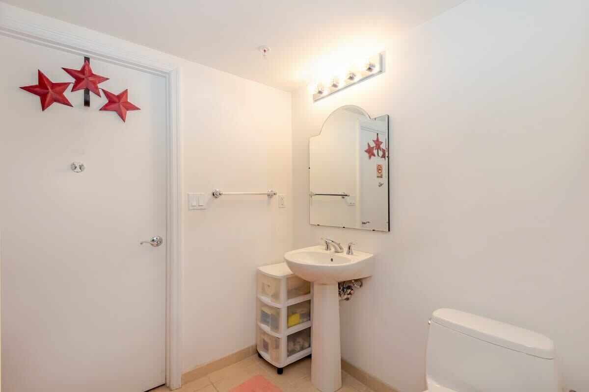 A small bathroom with a white sink, a mirror, and a toilet. There are three red star decorations on the wall.