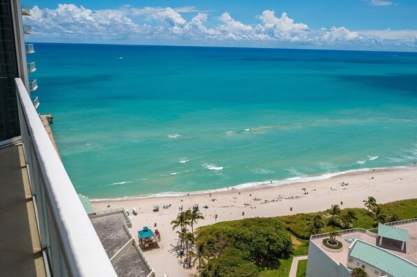 A beach view from a balcony with a clear sky and calm sea.