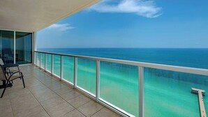 A balcony with a glass railing overlooking a turquoise sea and a clear sky.
