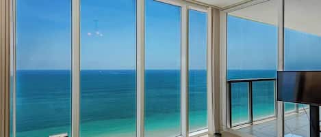 A spacious room with large floor-to-ceiling windows offering a view of the ocean.